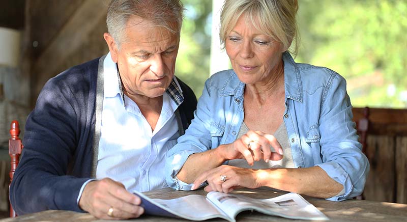 Senior couple in yard reading magazine